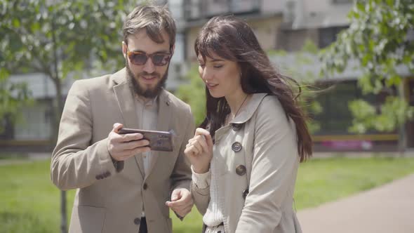 Smiling Caucasian Man and Woman with Smartphone Greeting Friend and Leaving. Portrait of Happy Adult