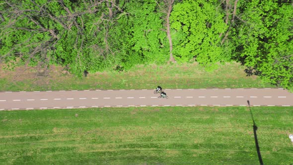 Cyclists Walk Along a Bike Path in the Middle of a Park Near Trees on a Spring Day