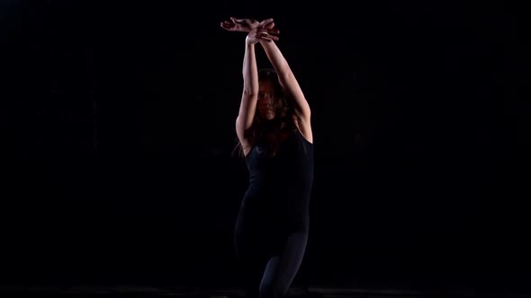 Young Energetic Woman in a Black Suit in the Studio on a Dark Background Dancing, Moving and Posing