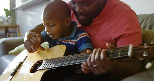 Father teaching his son how to play guitar at home 4k