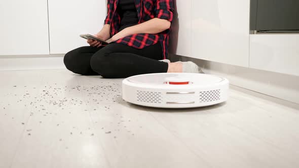 Woman with Smartphone Controls Robot Vacuum Cleaner at Home