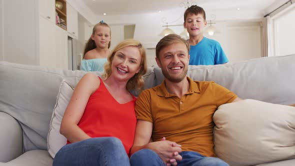 Portrait of happy caucasian parents, son and daughter sitting at home on sofa