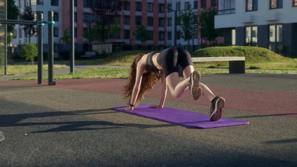Athletic Slender Girl in Black Tight Uniform Does Plank Run on Street on Sports Ground in