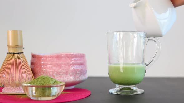 Person adding milk to glass with matcha