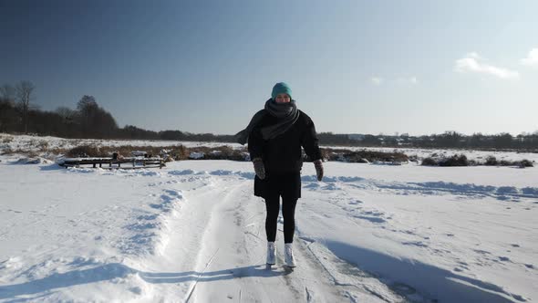 Young woman in black skirt and white figure skates is ice skating on frozen lake