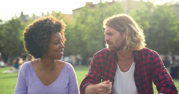 Romantic Multiracial Couple Sitting on Lawn in Park and Talking