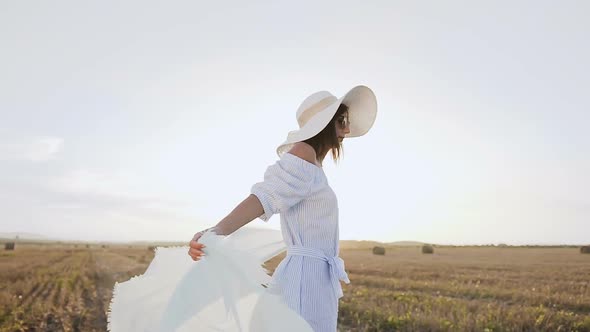 Attractive Girl in a Long Dress Sunglasses Big Hat with a Scarf Spins Around Herself
