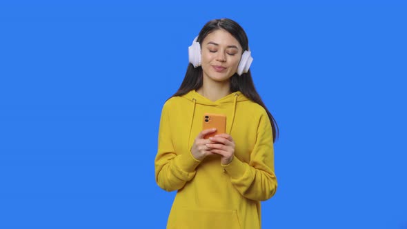 Portrait of Pretty Brunette Enjoying Music with Big White Headphones Using Phone