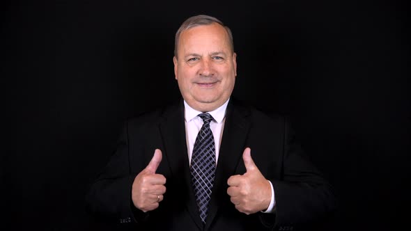 An Old Businessman in a Suit Shows Like with Two Hands. Isolated Black Background