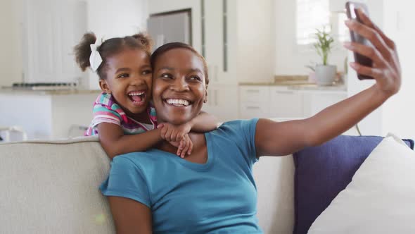 Happy african american mother and daughter taking selfie at home