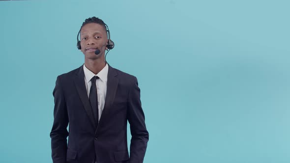 Black Man in an Office Suit and Headset Nods Positively to the Camera in a Blue Background