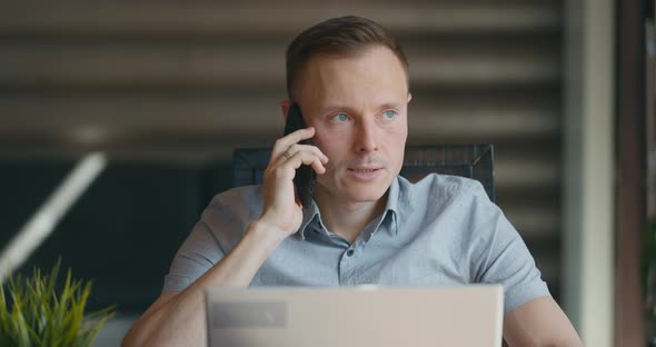 Man is Sitting Inroom at Laptop and Talking on the Phone