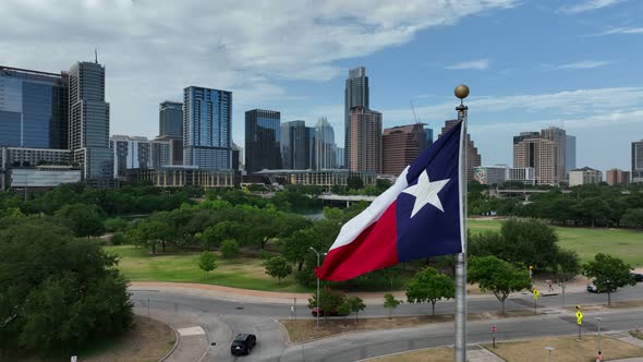 Rising aerial shot of Texas flag in front of Austin, Texas skyline. Walkable green space and park in