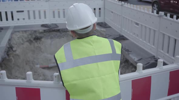 Cute Small Boy Wearing Safety Equipment and Constructor Helmet Standing on the Road and Checks Pit