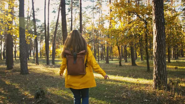 Young Lady in Parka Coat and Backpack is Walking By Autumn Wood Smiling and Spinning Around