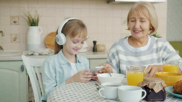 Slow Motion of Little Girl Using Smartphone and Listening To Music in Headphones at Kitchen Table