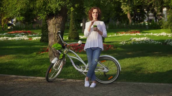 Beautiful Woman Standing in the City Park Near Her City Bicycle with Flowers in Its Basket and