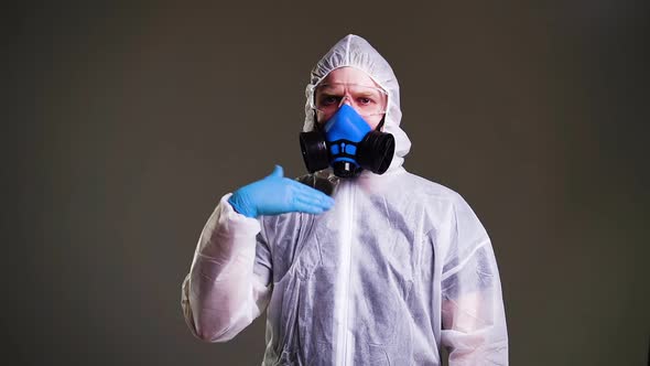 Doctor Wearing Protective Suit, Goggles and a Respirator Points Finger at Camera