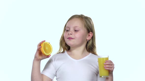 Little Girl Holds an Orange Slice and Licks It and Drinks Orange Juice, White Background, Slow