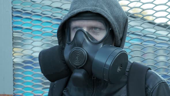 Man in Gas Mask Jacket with Hood Standing Outdoors in Front of Moving Train