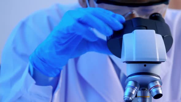 Asian scientist doing some research and looking through a microscope in laboratory.