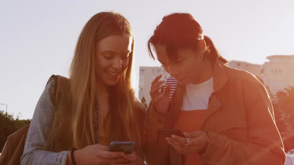 Side view of a Caucasian and a mixed race girl using their phone