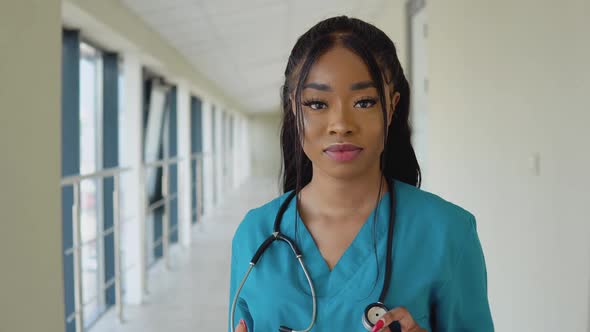 Young African American Female Doctor in a Blue Suit and with a Stethoscope Stands in the Corridor of