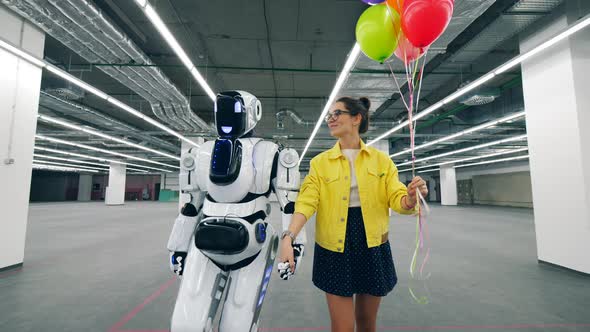 Tall Robot Is Walking with a Young Woman Talking To It