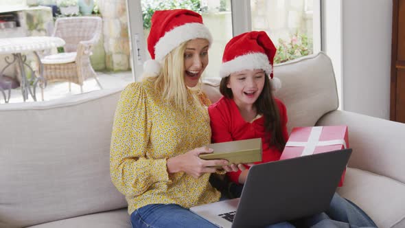 Mother and daughter holding gift boxes while having a video chat on laptop at home