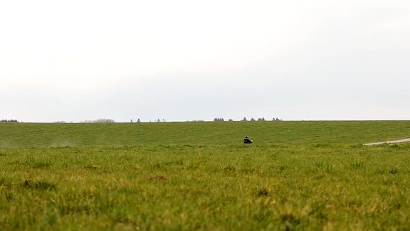 Person on a dirt bike riding along a dirt road stirring up dust in the distance. Static wide angle v