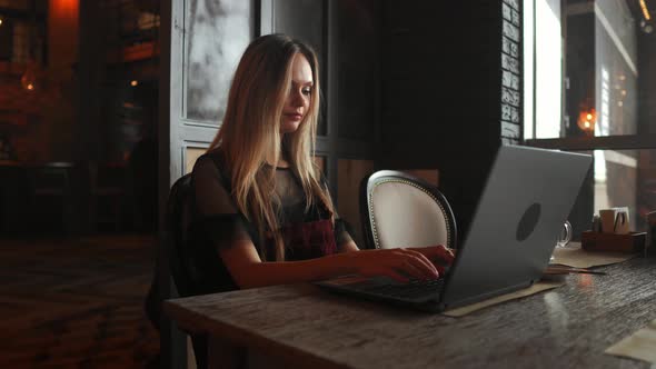 Side View. Young Business Woman Sitting at Table and Taking Notes in Notebook