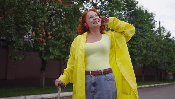 Portrait of Joyful Redhead Retro Woman in Yellow Rain Coat Singing Listening to Music in Headphones