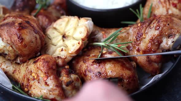 Cutting Baked Spicy Chicken Legs with Rosemary and Garlic on Black Slate, Dark Background.