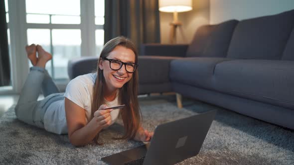 Woman Is Lying on the Floor and Makes an Online Purchase Using a Credit Card and Laptop. Online