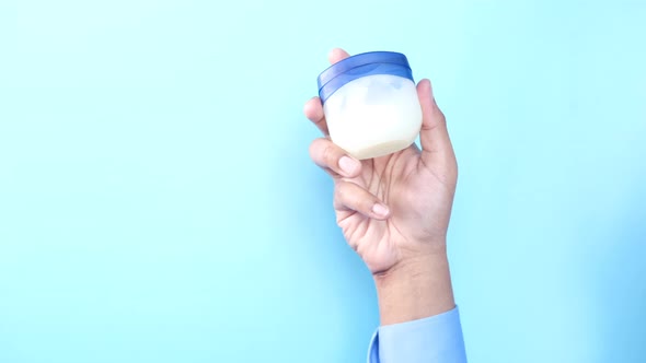 Man Hand Holding Petroleum Jelly Against Blue Background