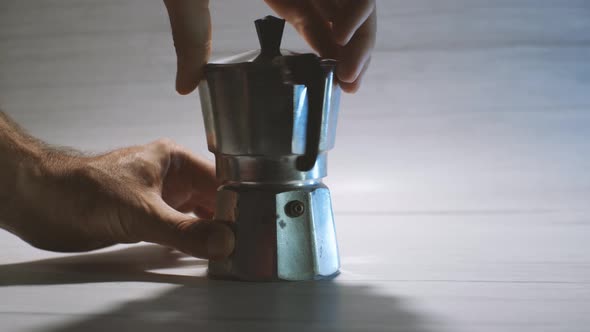 A man's hands dismantle a geyser coffee maker to make coffee