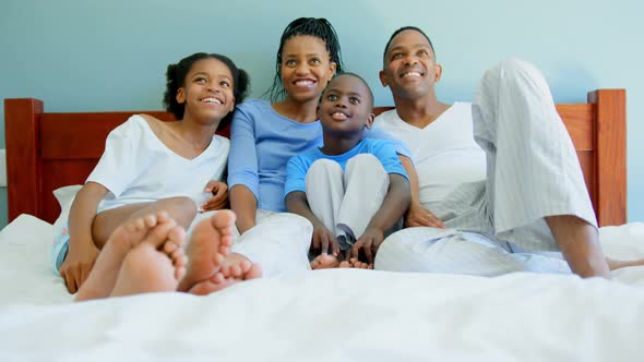 Front view of young black family watching television on bed in bedroom of comfortable home 4k