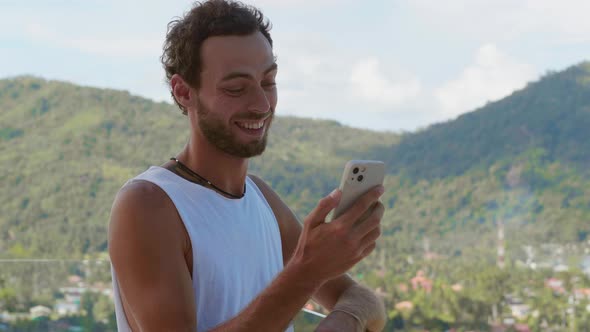 Cheerful Guy in White Tshirt Using His Mobile Phone and Chatting By Video Link with His Interlocutor