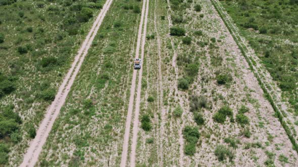 Aerial Of A Safari Land Rover Driving Across Fence Line Savannah Of Central Kalahari Game Reserve, B