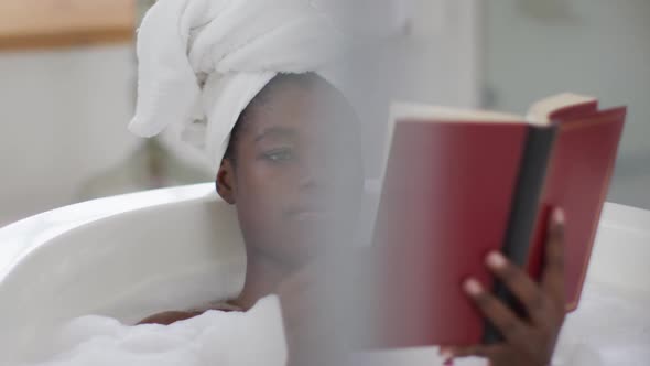 Portrait of african american attractive woman relaxing in bath and reading book in bathroom
