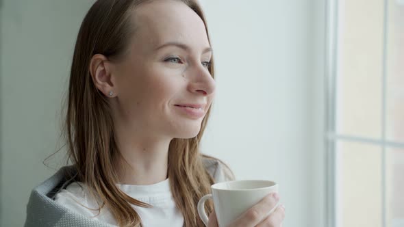 Woman Thinking Holding a Mug Beside a Window at Home
