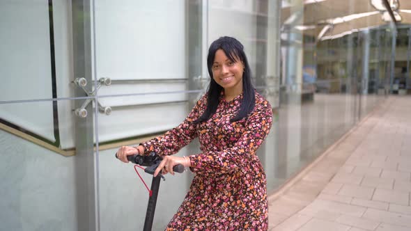 Smiling ethnic woman riding electric scooter in office building