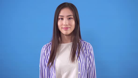Portrait of a Young Asian Woman in a Shirt Stands on a Blue Background