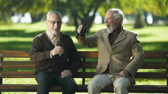 Two Happy Senior Friends Clinking Beer Bottle in Park, Remembering Young Ages