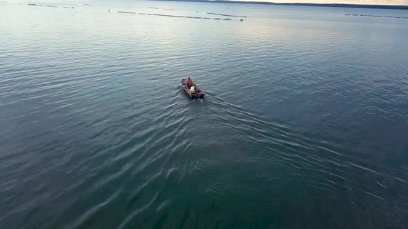 Aerial drone shot flying over two fishermen in a small fishing boat on a lake on a fishing farm in B