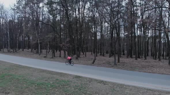 Professional cyclist on road bike is hard pedalling and sprinting. Woman cycling in forest on road