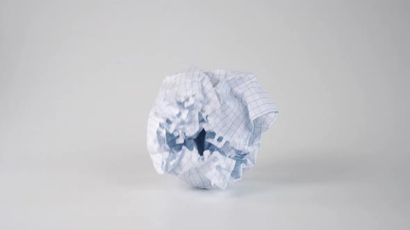 Thrown crumpled paper ball falls and rolls on a white surface in slow motion