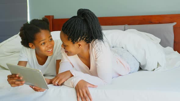 Front view of mid adult black mother and daughter using digital tablet on bed in comfortable home 4k