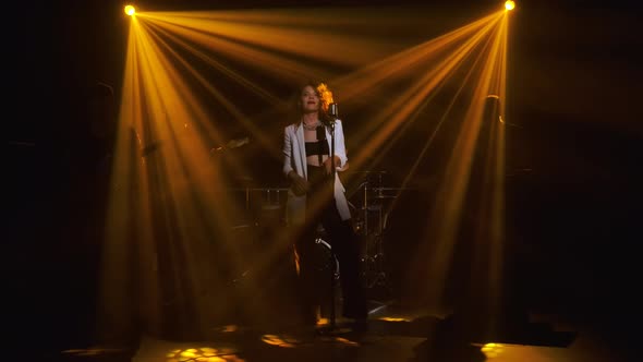 A Stylish Girl Vocalist Sings on Stage in a Vintage Microphone. In the Background Musicians