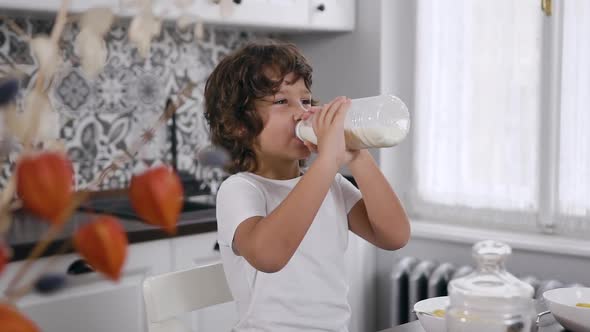 Handsome and Cute Little Boy Sitting at Kitchen Table and Drink Milk in the Home Kitchen